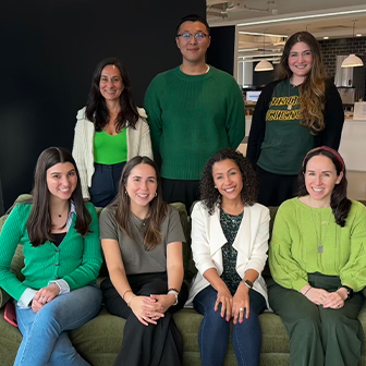 Photo with 4 people sitting on a couch and 4 people standing behind them smiling, all are wearing green